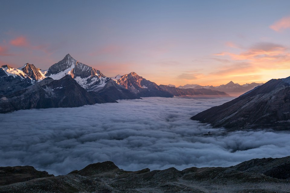 Snowy peaks above clouds at sunset